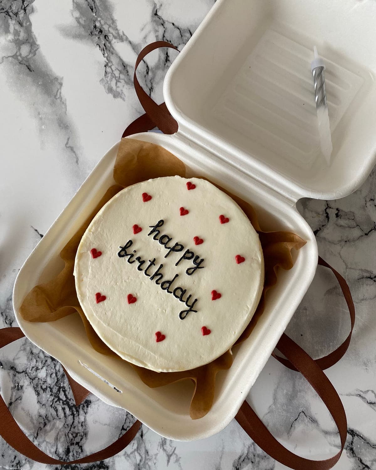 Small bento cake piped with hearts and lettering inside a kraft gift box