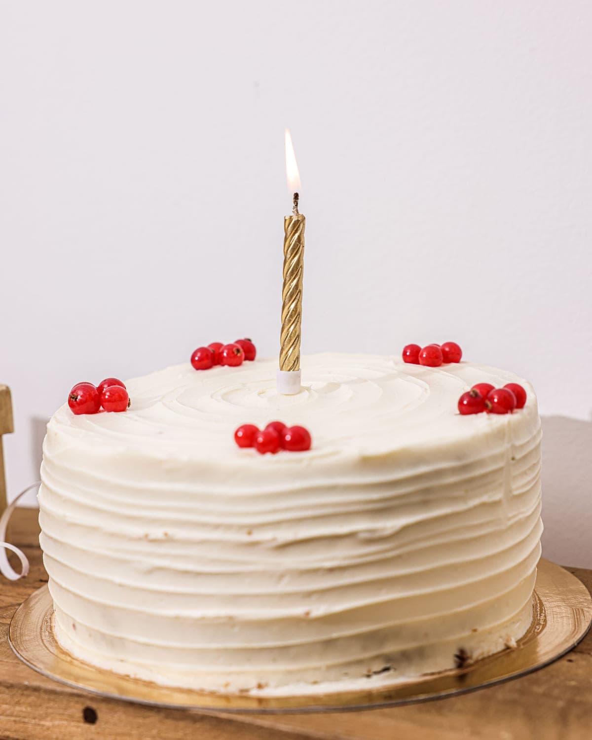 Ivory buttercream cake with red currants and a slim gold candle