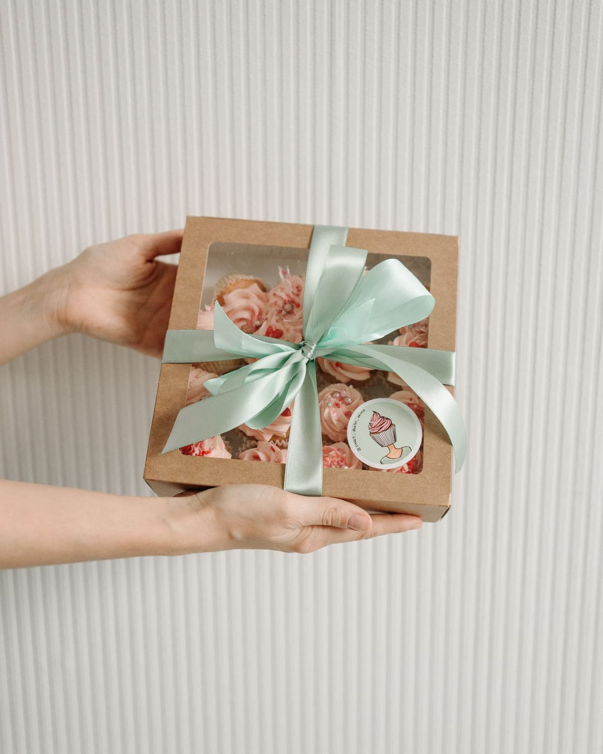 Gift box of frosted cupcakes tied with a pastel ribbon