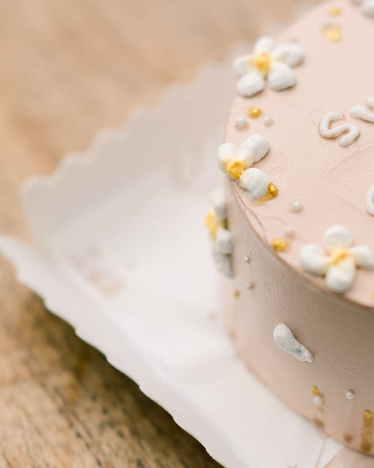 Pastel pink cake hand-piped with blossoms, pearls and custom lettering
