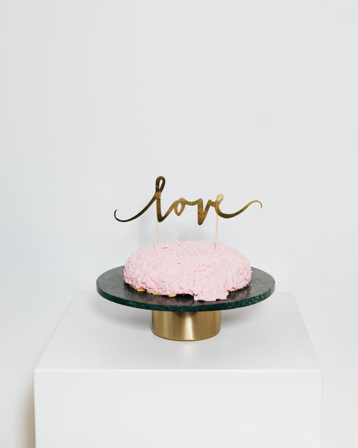 Small pink cake with a gold topper on a glass cake stand