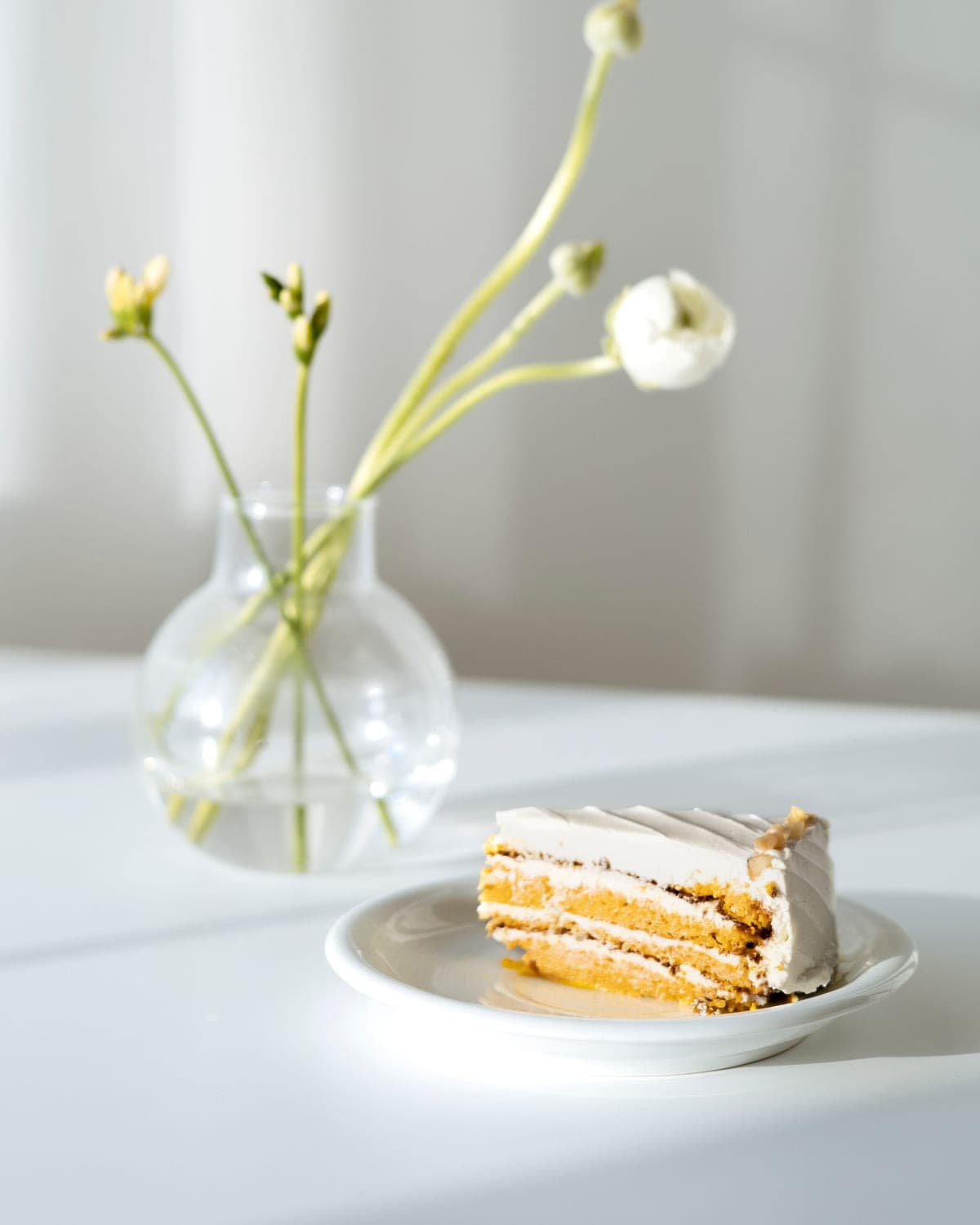 Slice of layer cake on a saucer beside a small vase of flowers